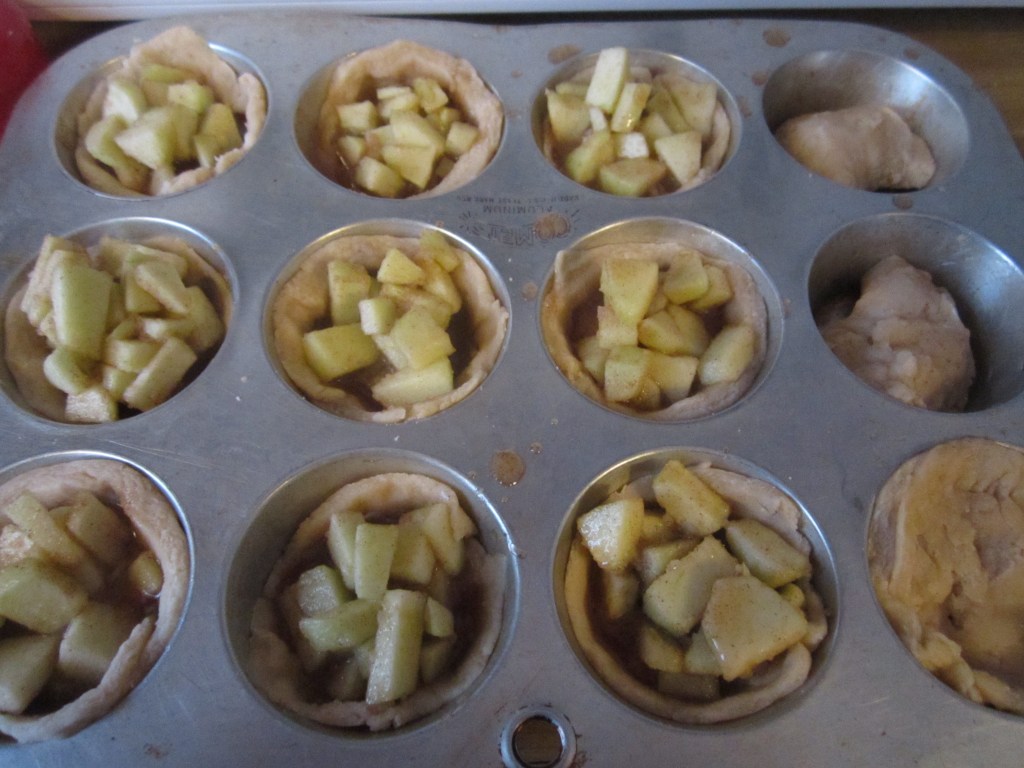 Picture of a muffin tin filled to the brims with dough and apple pie filling.