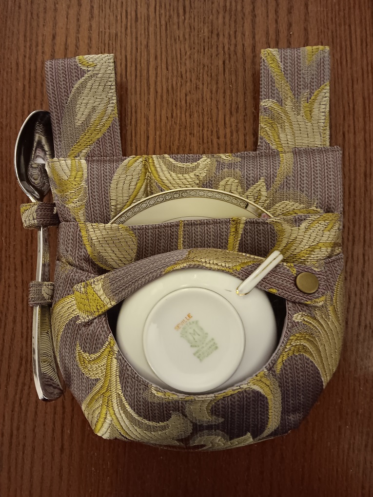 A purple and yellow teacup holster complete with teacup, saucer, and spoon.